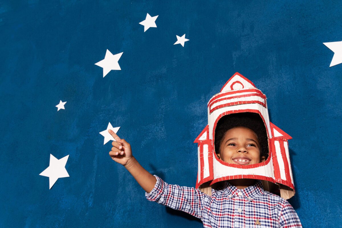 A young boy wearing a paper rocket, fascinated by the sky.