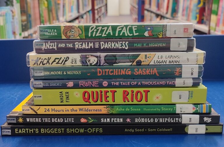 A stack of ten children's and young adult books lies on a blue surface, inviting young readers to explore, with bookshelves and library aisles visible in the background.