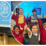 Five children in school uniforms give thumbs up in a classroom, standing before a screen announcing I Follow the Fox by Rob Biddulph as the winner of the Harrow Picture Book Award.